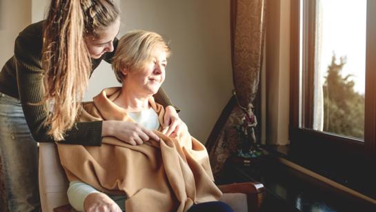 Young Carer Helping Woman With Clothing