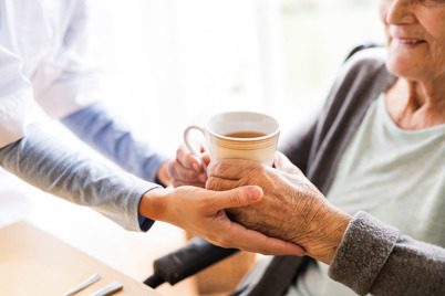 Lady being handed a cup of tea by carer